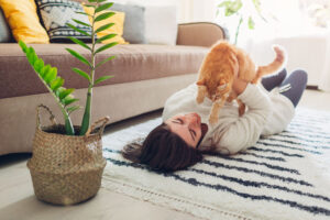 young woman playing with cat on carpet with plant behind them